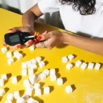 Close-up of a person testing blood sugar levels with a glucometer surrounded by sugar cubes.