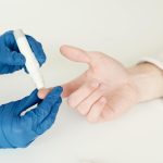 A healthcare professional tests blood sugar with a glucometer and lancet pen in a medical setting.