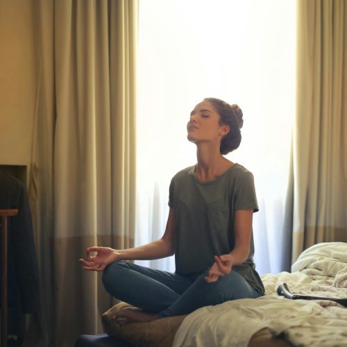 Adult woman practicing meditation on her bed surrounded by a calm bedroom atmosphere.